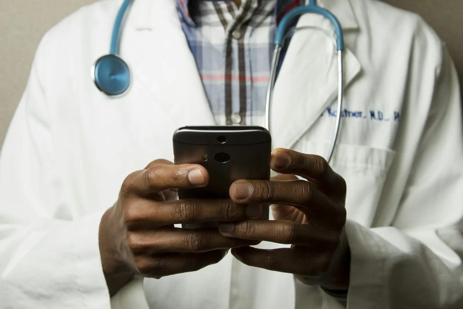A doctor in a white coat with a stethoscope, using a phone