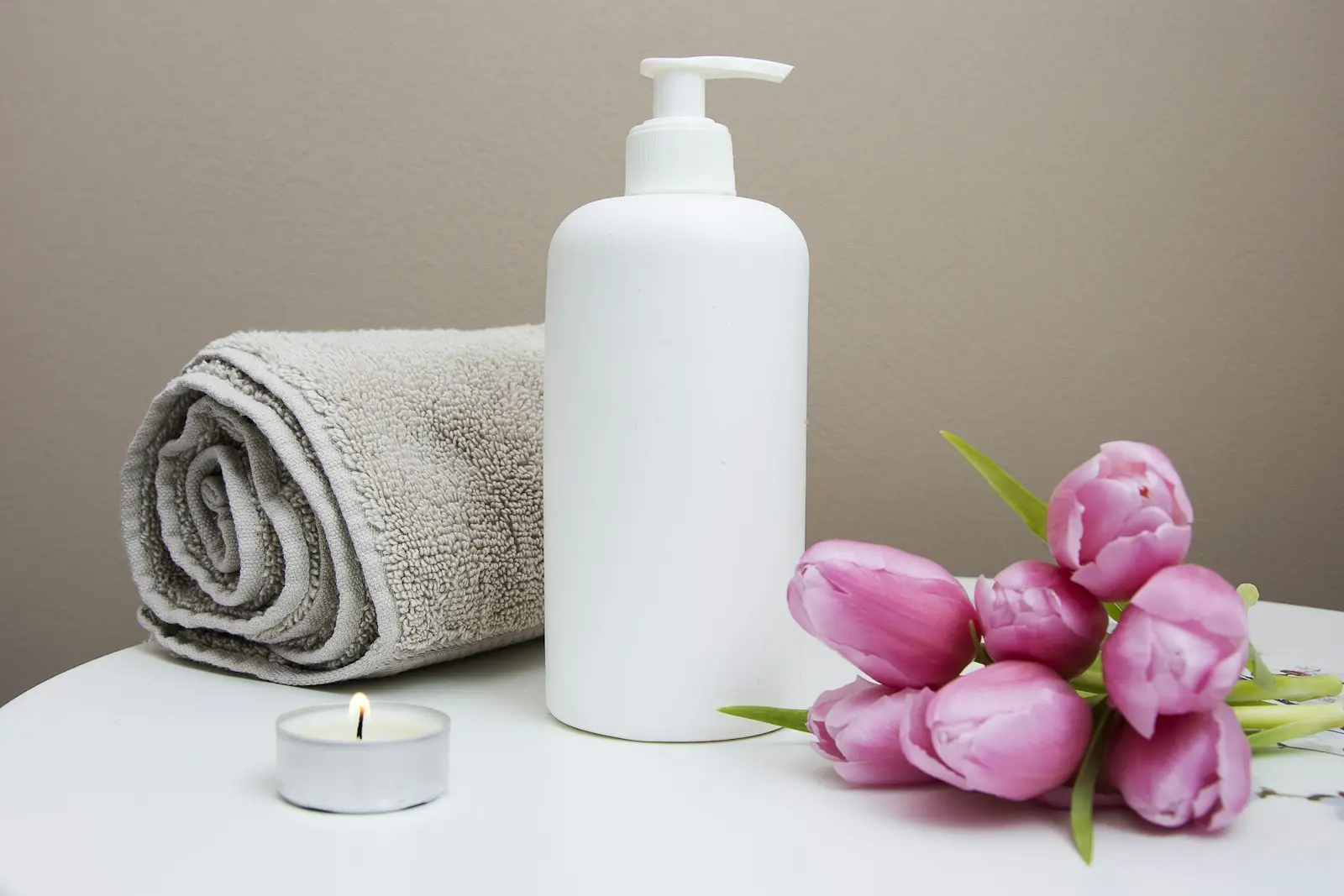 Spa products, a rolled towel, a candle and pink tulips on a table